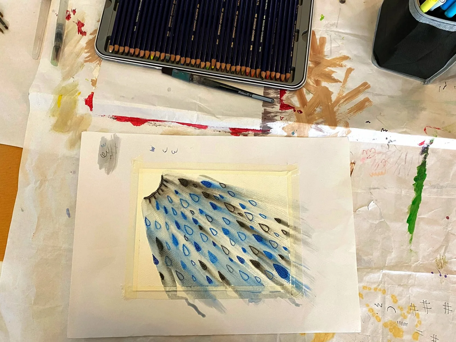 用色鉛筆畫的毛衣局部，佈滿藍色與深色水滴圖案，桌上擺著一盒色鉛筆